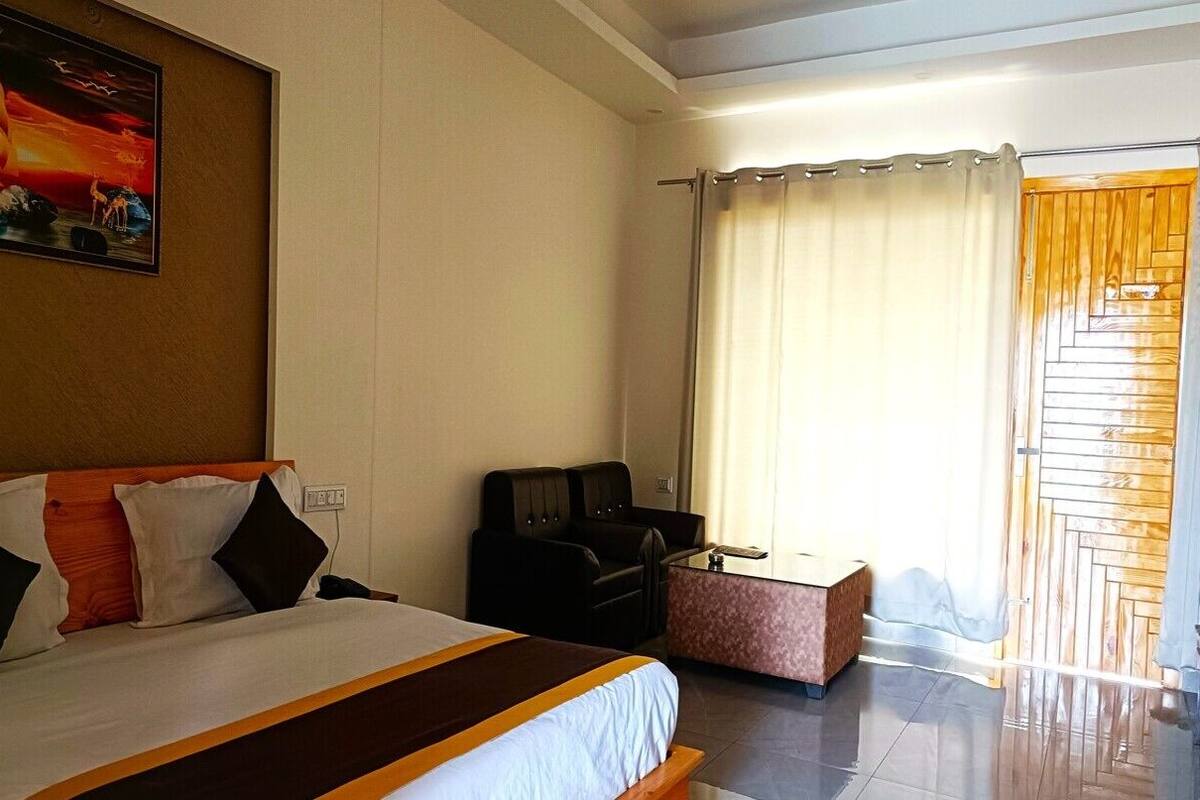 A hotel room with a bed, a desk, a chair, and a view of the outside through a window with curtains.