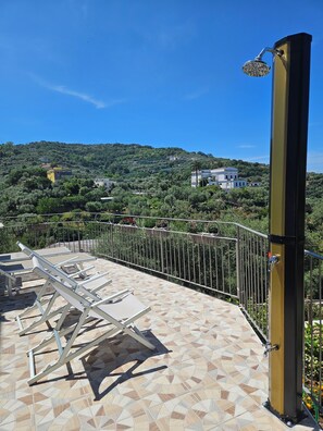 Una terraza con barandilla metálica, una fuente de agua y vistas a una colina con edificios.