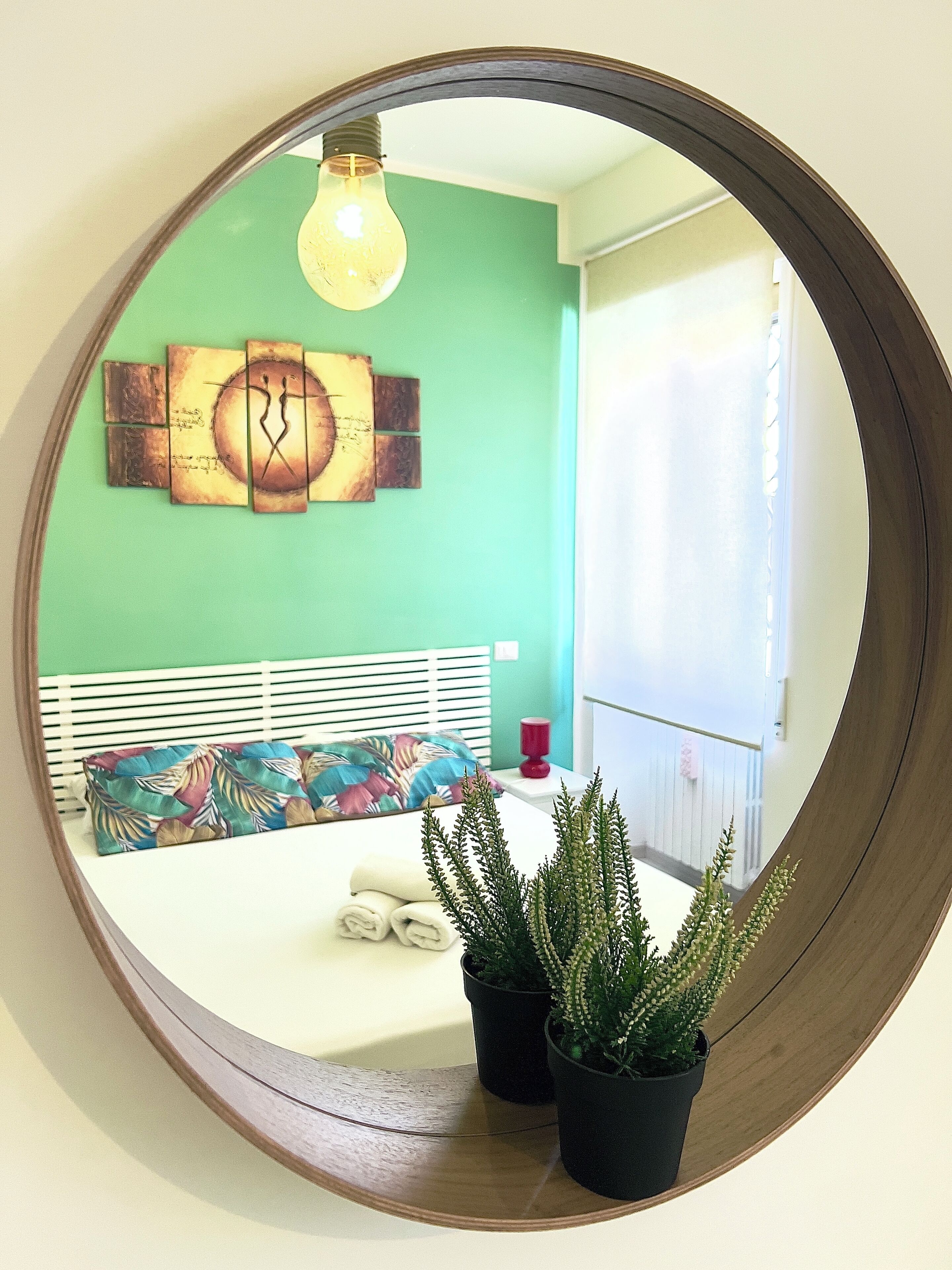 A bedroom with a bed, a mirror, a wall clock, and two potted plants.