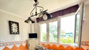 A kitchen with a dining table, chairs, a clock, and a window with a view of greenery. - Casa Montañesa al Lado de la Playa (Somo)