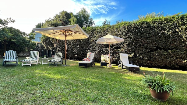 A backyard with four striped lounge chairs, two umbrellas, and a potted plant. - Casa Montañesa al Lado de la Playa (Somo)