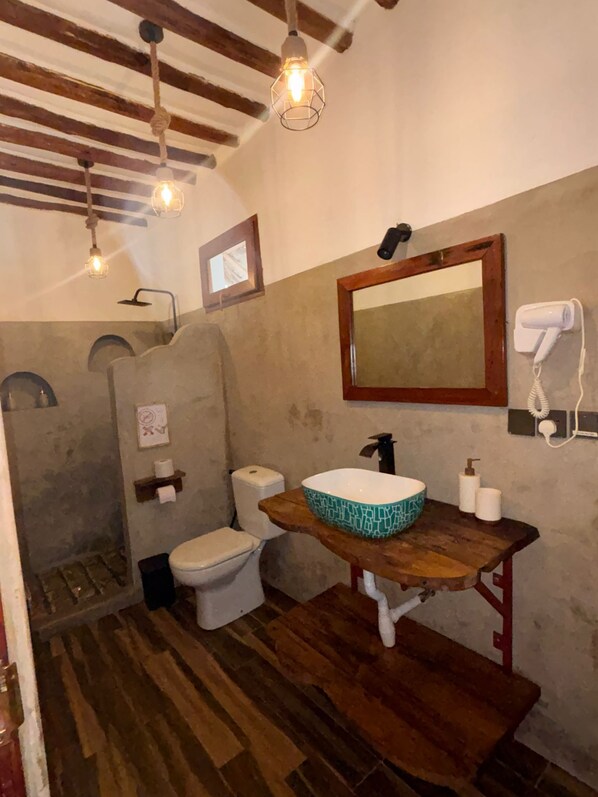A bathroom with a wooden vanity, a large mirror, a towel rack, a hairdryer, and a shower area.