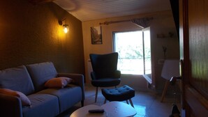 A living room with a sofa, a chair, a small table, and a window with a view of trees. - Tramontane, bedroom, and TV room. Near Avignon. (Jonquerettes)