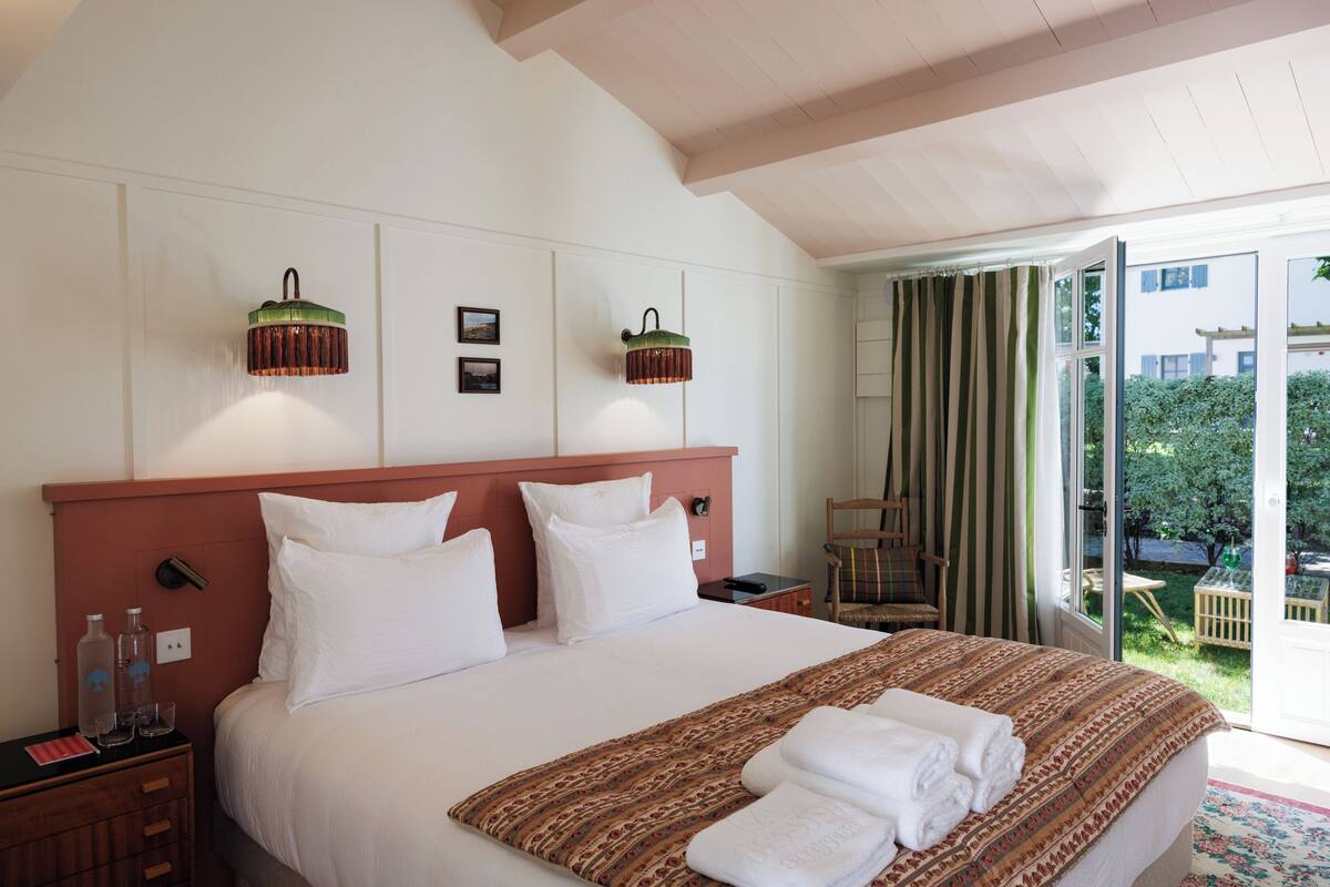 Una habitación de hotel con una cama grande, dos lámparas fijadas a la pared, una mesita de noche de madera y vistas al exterior.