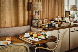 A breakfast setup with a wooden table, wicker chairs, and a variety of breakfast items including bread, pastries, and beverages. - Hotel La Mission  (Île d'Yeu)