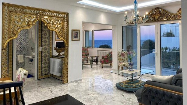 A spacious living area with a large window, a chandelier, and a view of the sea. - Luxurious Sea View With Private Beach in Gammarth Marsa (La Marsa)
