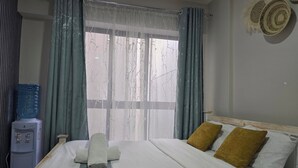 A hotel room with a bed, two pillows, a water dispenser, and a window with curtains. - Jali Stays, Serenity in Nairobi City (Nairobi)