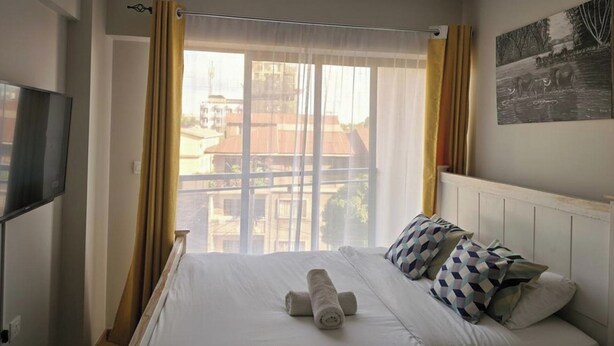A hotel room with a bed, a TV, a window with curtains, and a wall with a picture. - Jali Stays, Serenity in Nairobi City (Nairobi)