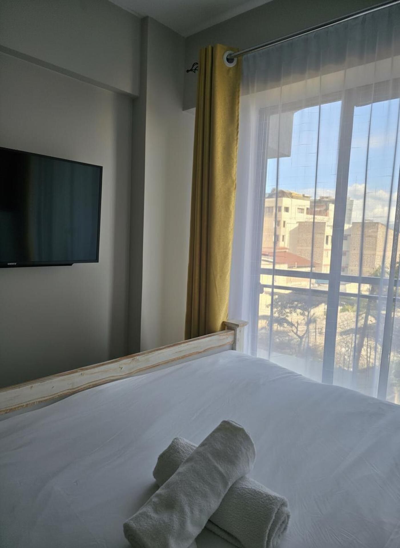 Habitación de hotel con una cama, un televisor montado en la pared y una ventana con cortina.
