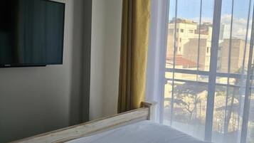 Habitación de hotel con una cama, un televisor montado en la pared y una ventana con cortina.