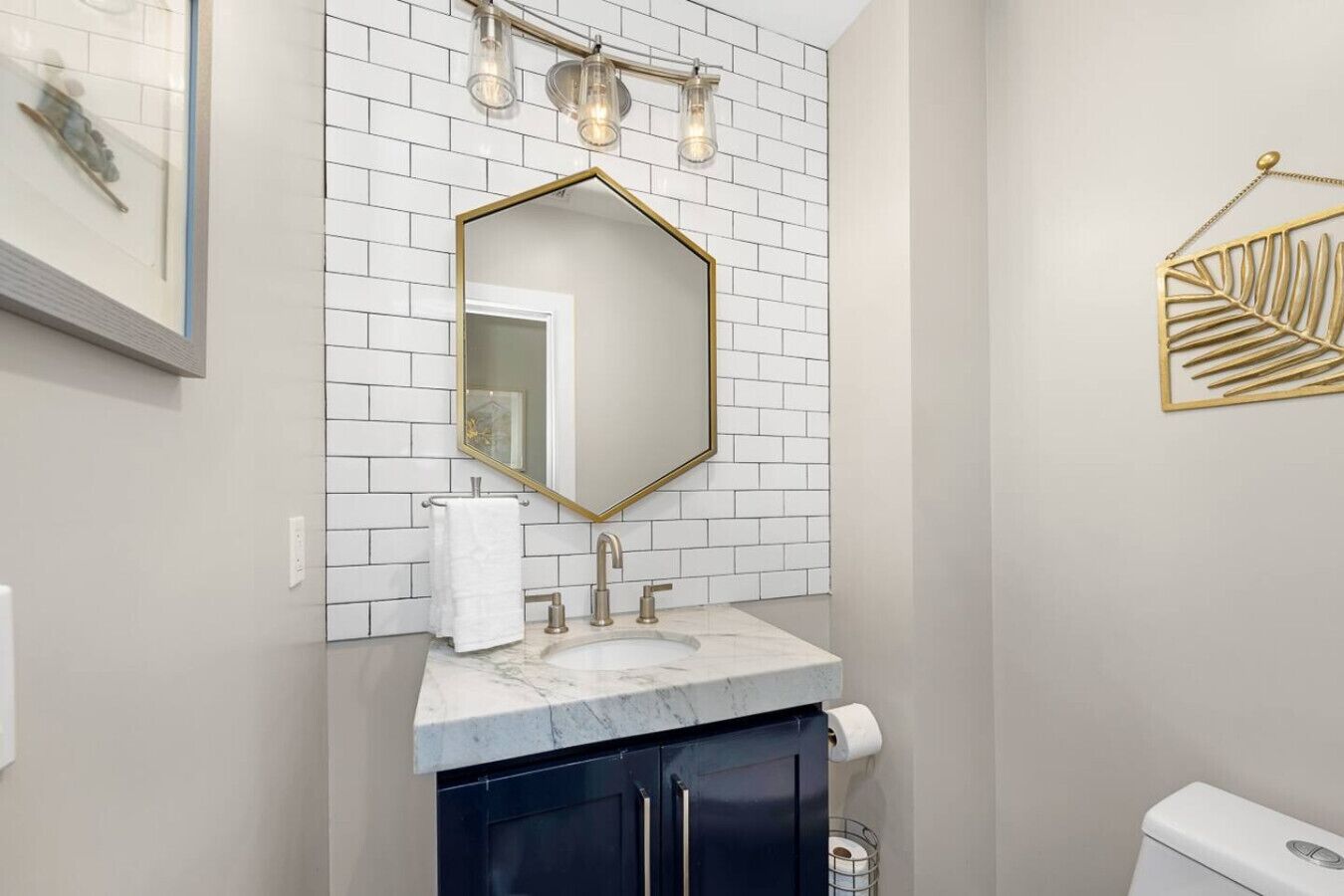 A bathroom with a white tiled wall, a gold-framed mirror, a marble sink, and a toilet.