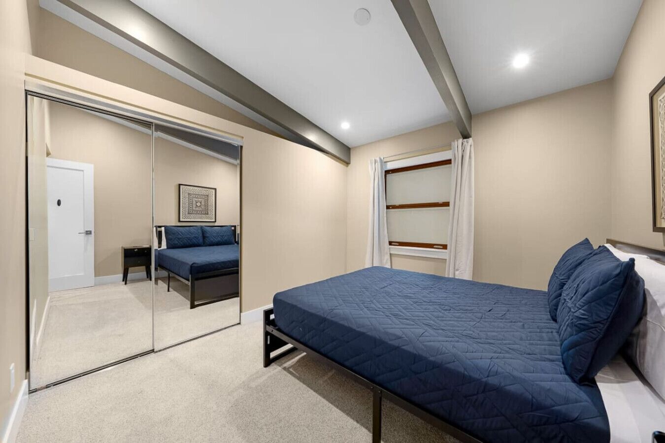 Un dormitorio con cama, armario, espejo y ventana con cortinas.