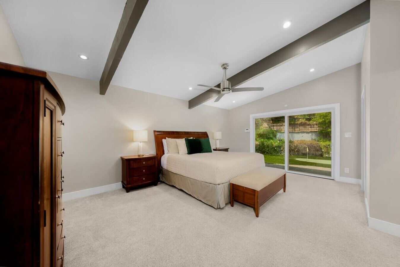 A bedroom with a bed, bedside tables, a ceiling fan, and a sliding glass door leading to a garden.