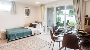 Un dormitorio moderno con cama, un área de comedor con sillas y una mesa, y un puerta corrediza de vidrio que da a un balcón.