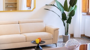 A living room with a beige sofa, a small round table with two cups, a large potted plant, and a mirror on the wall. - Singer House in Center Town (Lucca)