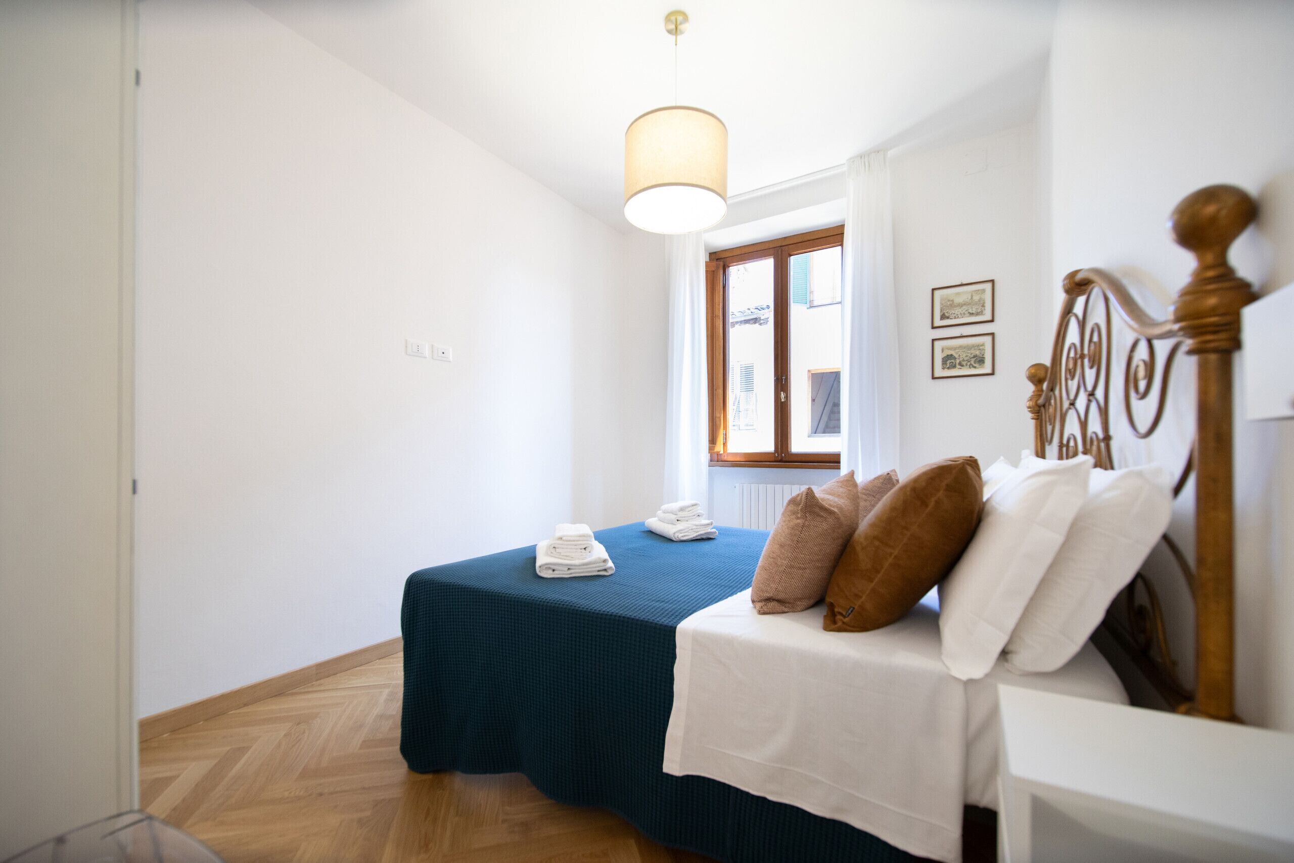 A bedroom with two beds, a wooden floor, a window with curtains, and a hanging light fixture.