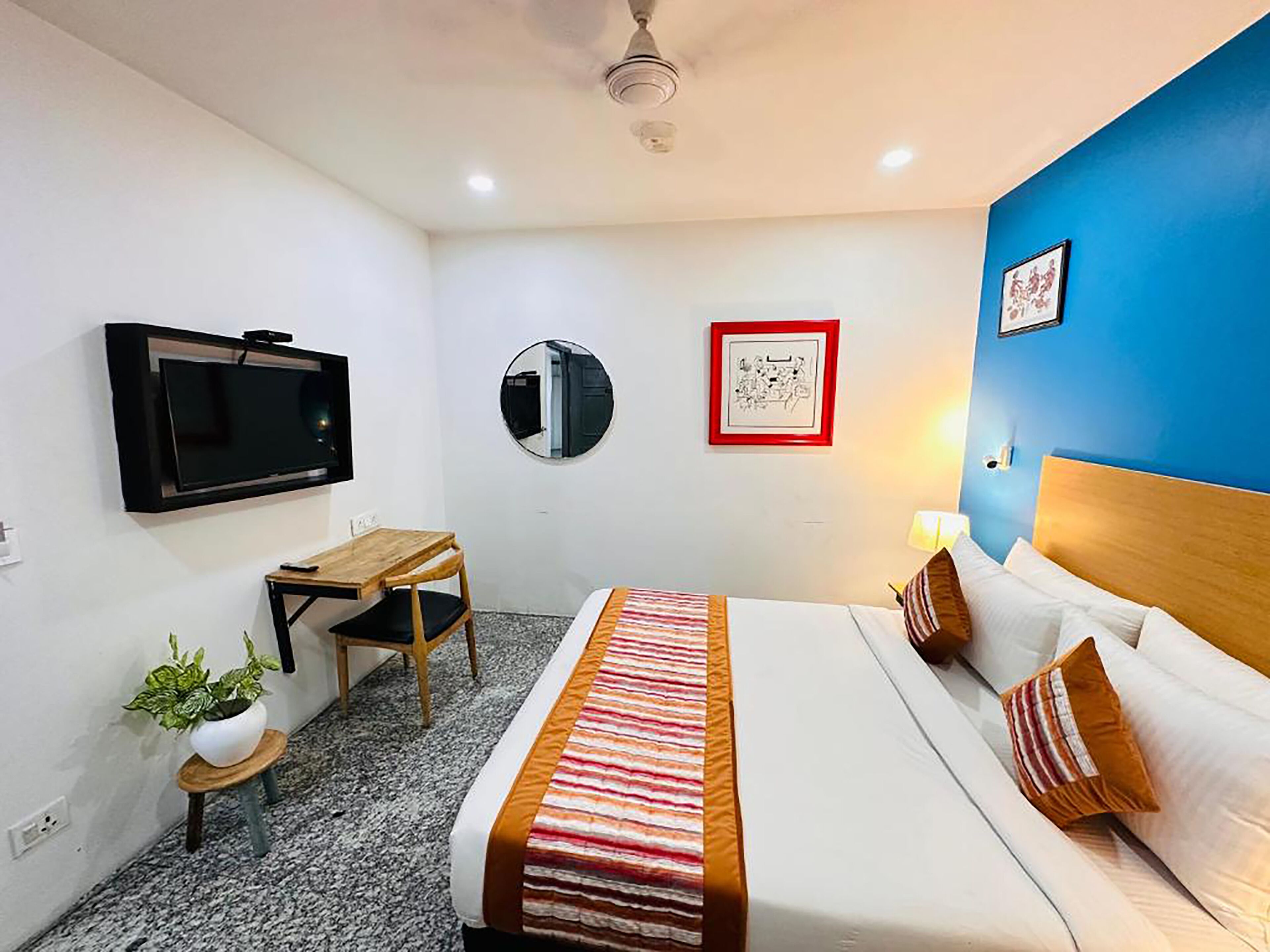 Une chambre d’hôtel avec un lit, un bureau, une télévision, un miroir et un mur orné d’un tableau.