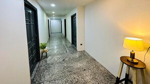 A hallway with a marble floor, black doors, and a lamp on the right. - Qotel Comfort Golden Saffron Punjabi Bagh (New Delhi)