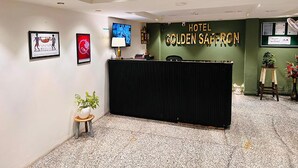 A hotel reception area with a black counter, framed artwork on the walls, a television, and a green wall with the hotel name. - Qotel Comfort Golden Saffron Punjabi Bagh (New Delhi)