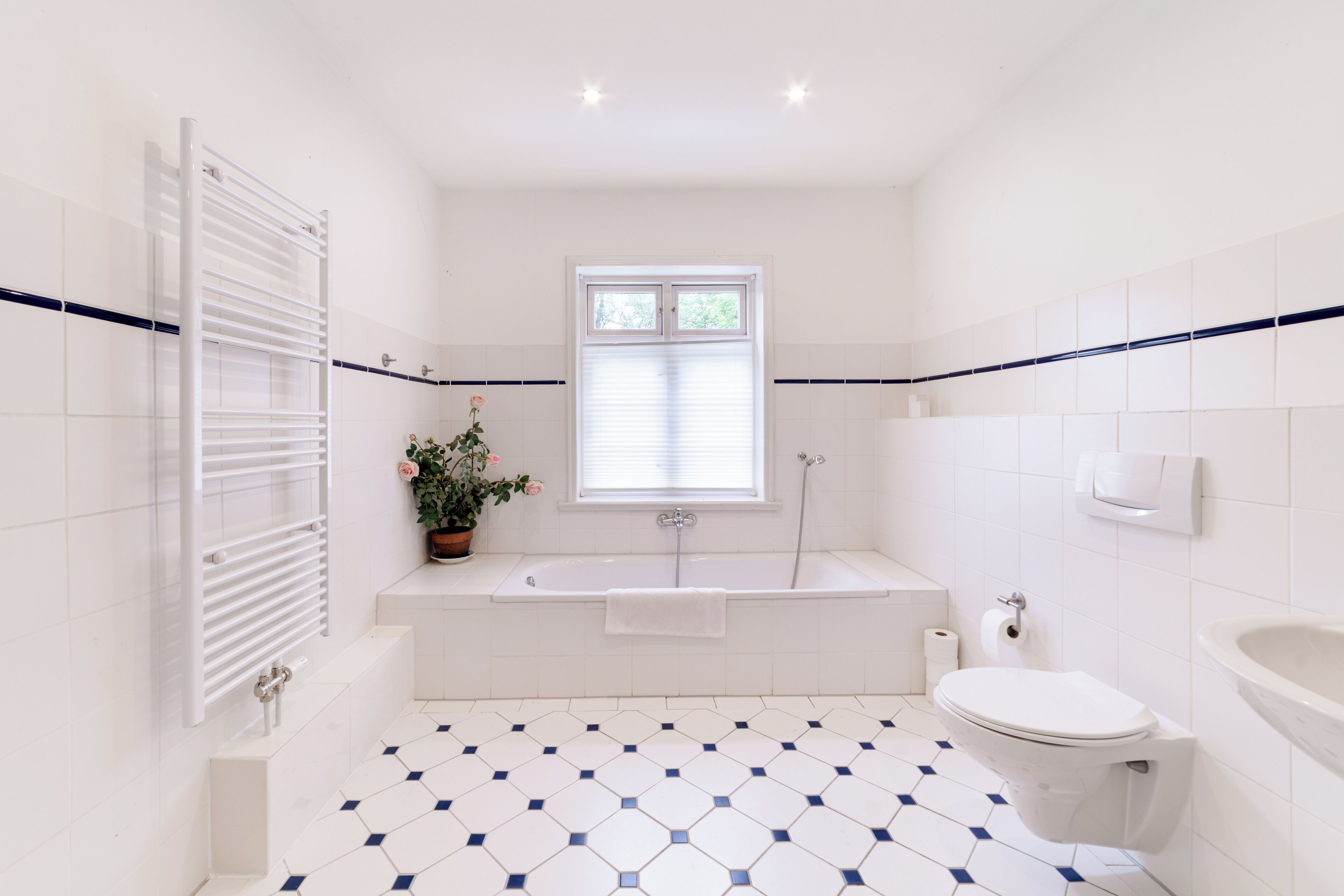 A bathroom with a white bathtub, toilet, and sink, a potted plant, and a window with blinds.