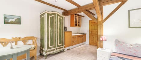 A bedroom with a wooden ceiling, a green wardrobe, a wooden cabinet, a white bedside table, and a bed with a floral-patterned bedspread.
