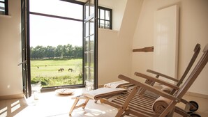 Una habitación con un ventanal grande, una silla de madera, una mesita con una cesta y un vaso de agua.