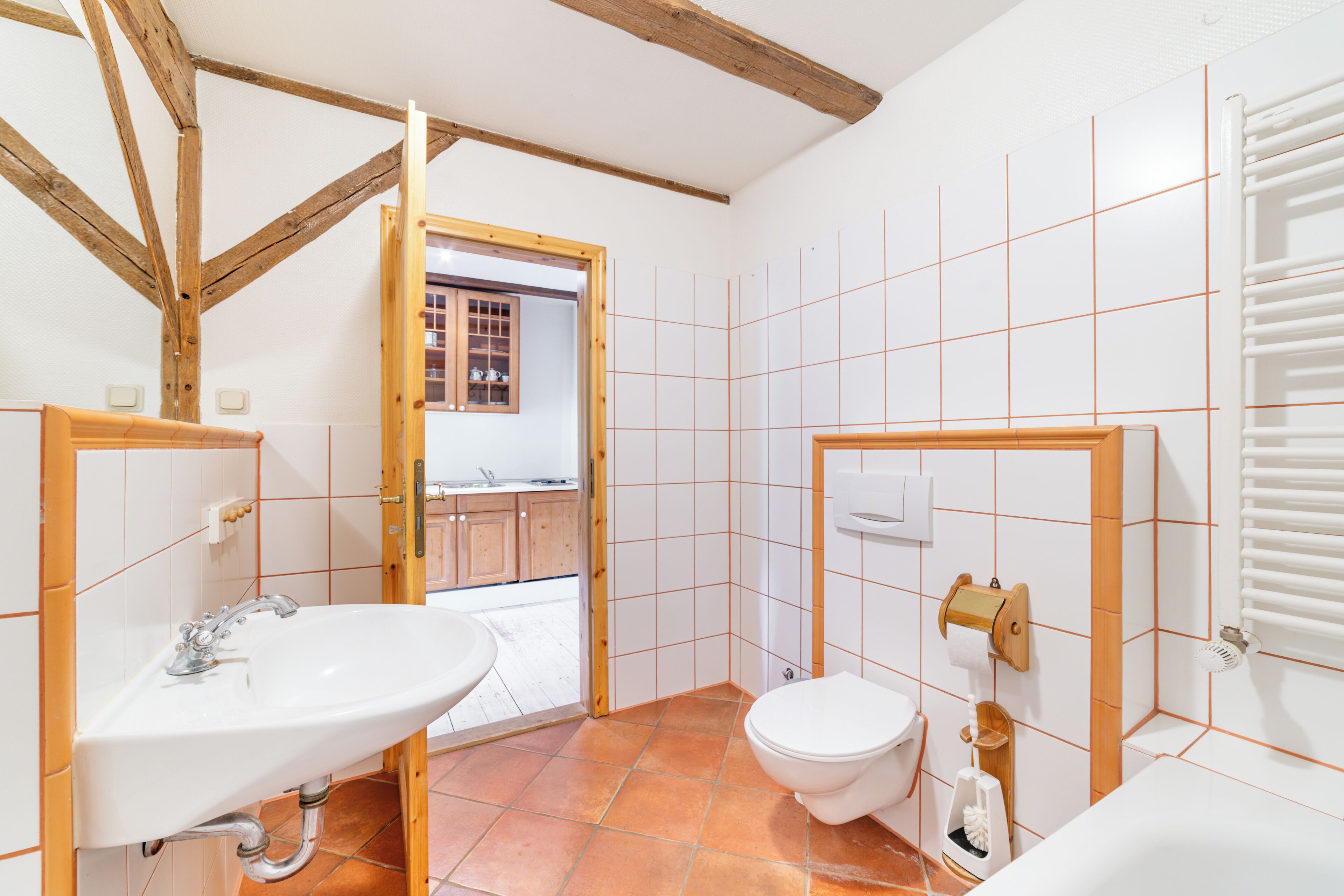 Une salle de bain avec un plafond en poutres apparentes, un lavabo, des toilettes et un espace douche.