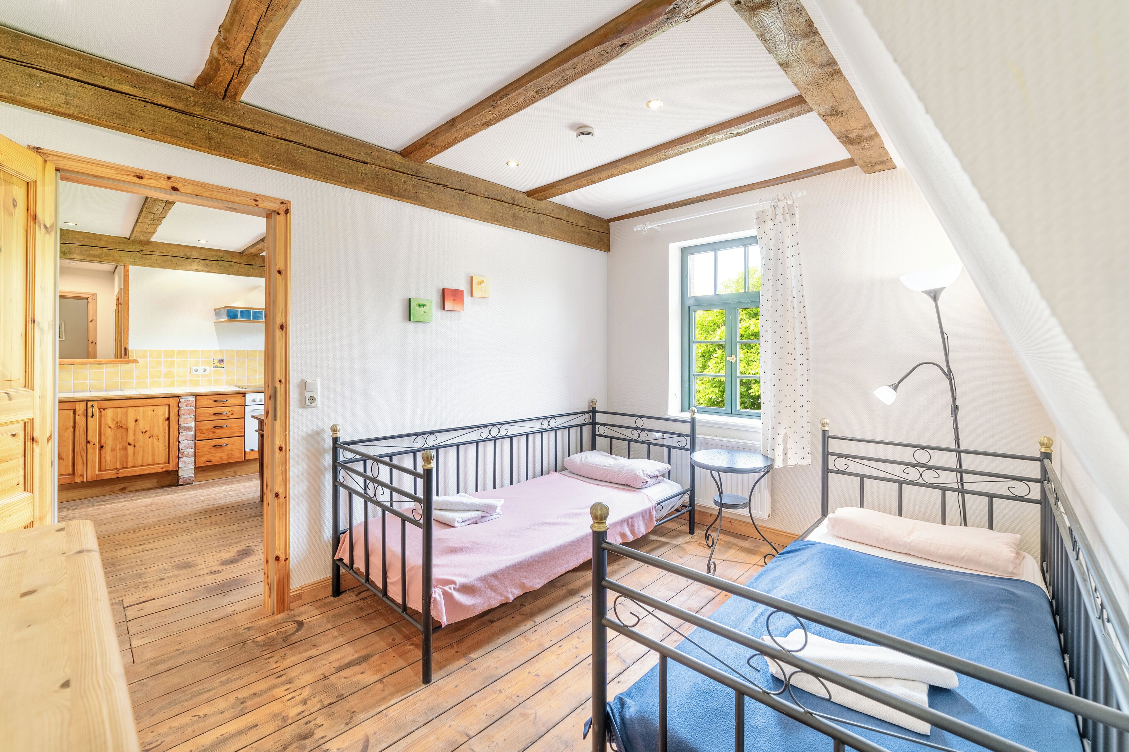 A bedroom with two beds, wooden floors, a small window, and a view of the outdoors.