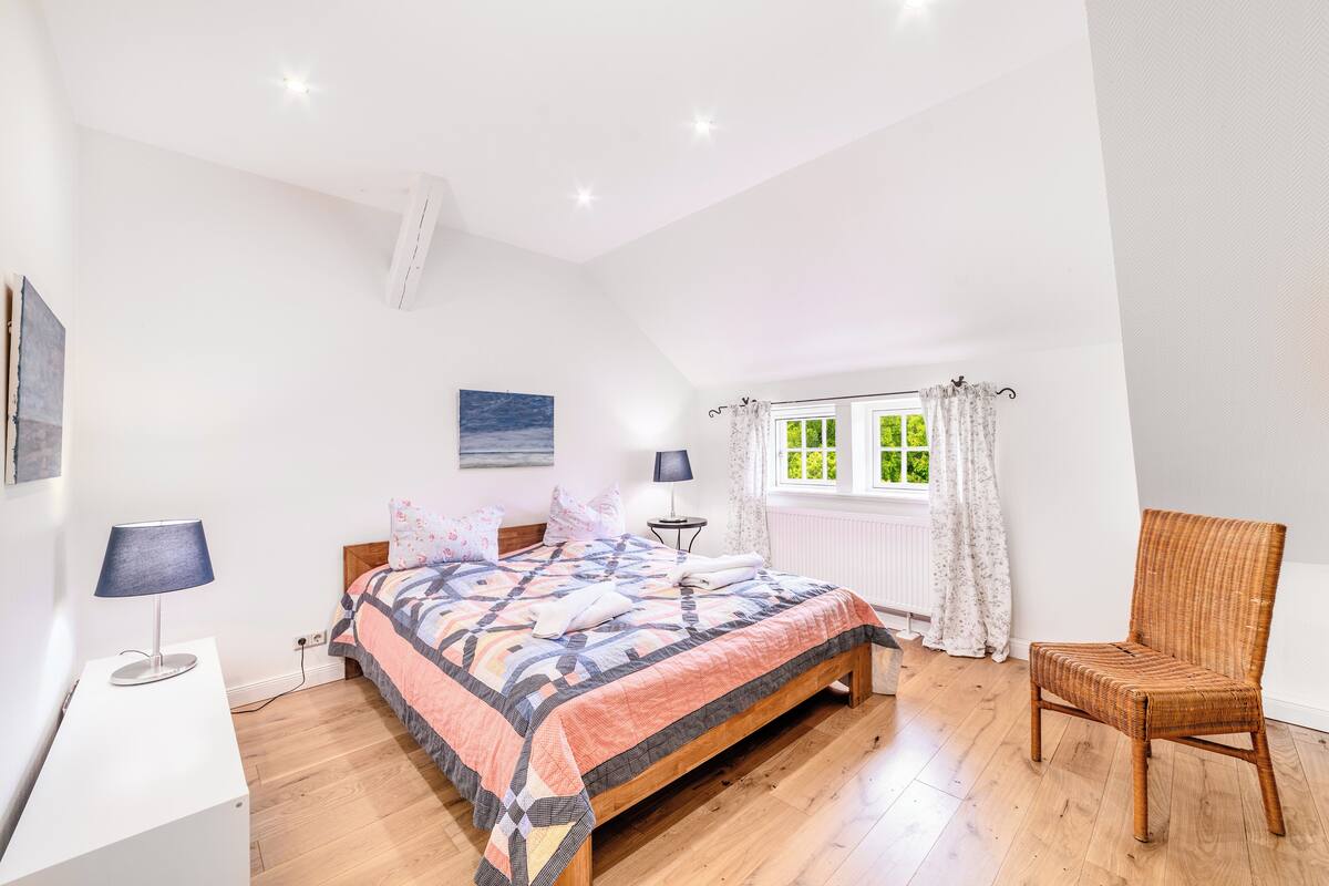 A bedroom with a bed, a chair, a desk, a window, and a painting on the wall.