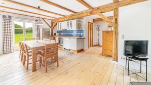 Una cocina amplia con vigas de madera, un comedor con mesa y sillas, y un televisor sobre un mueble.