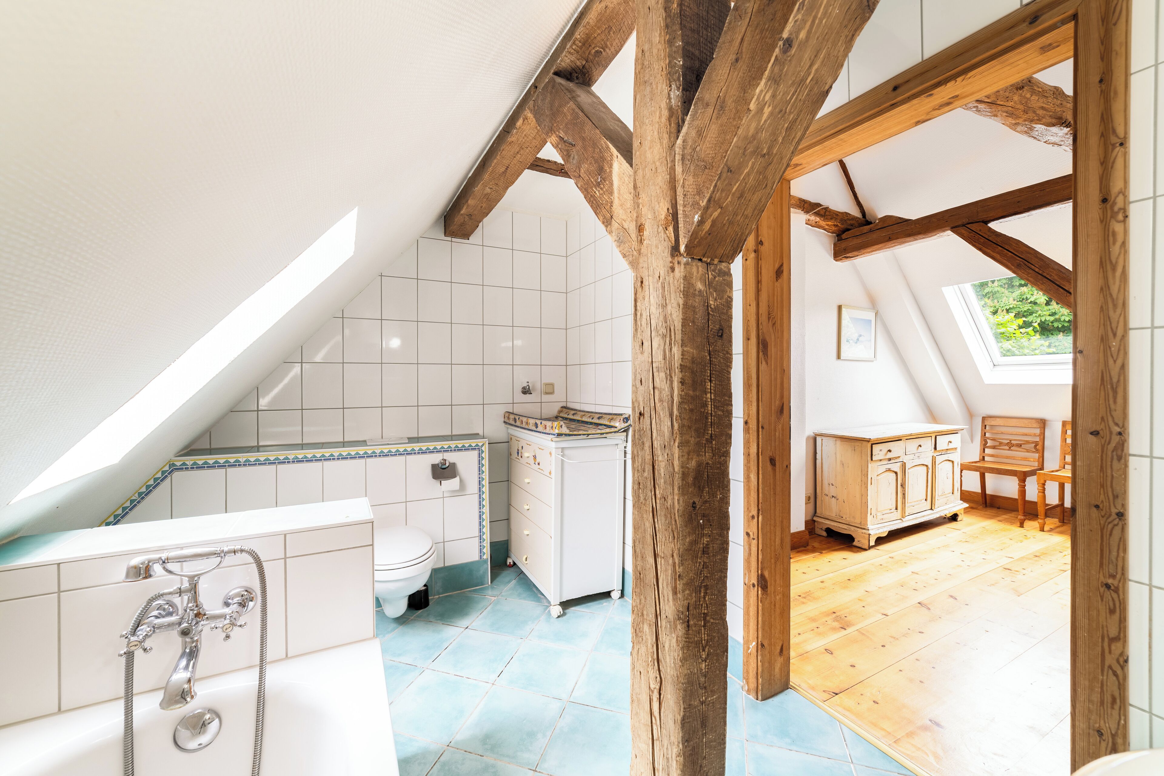A bathroom with a bathtub, toilet, and sink, wooden beams, and a view of the outdoors.