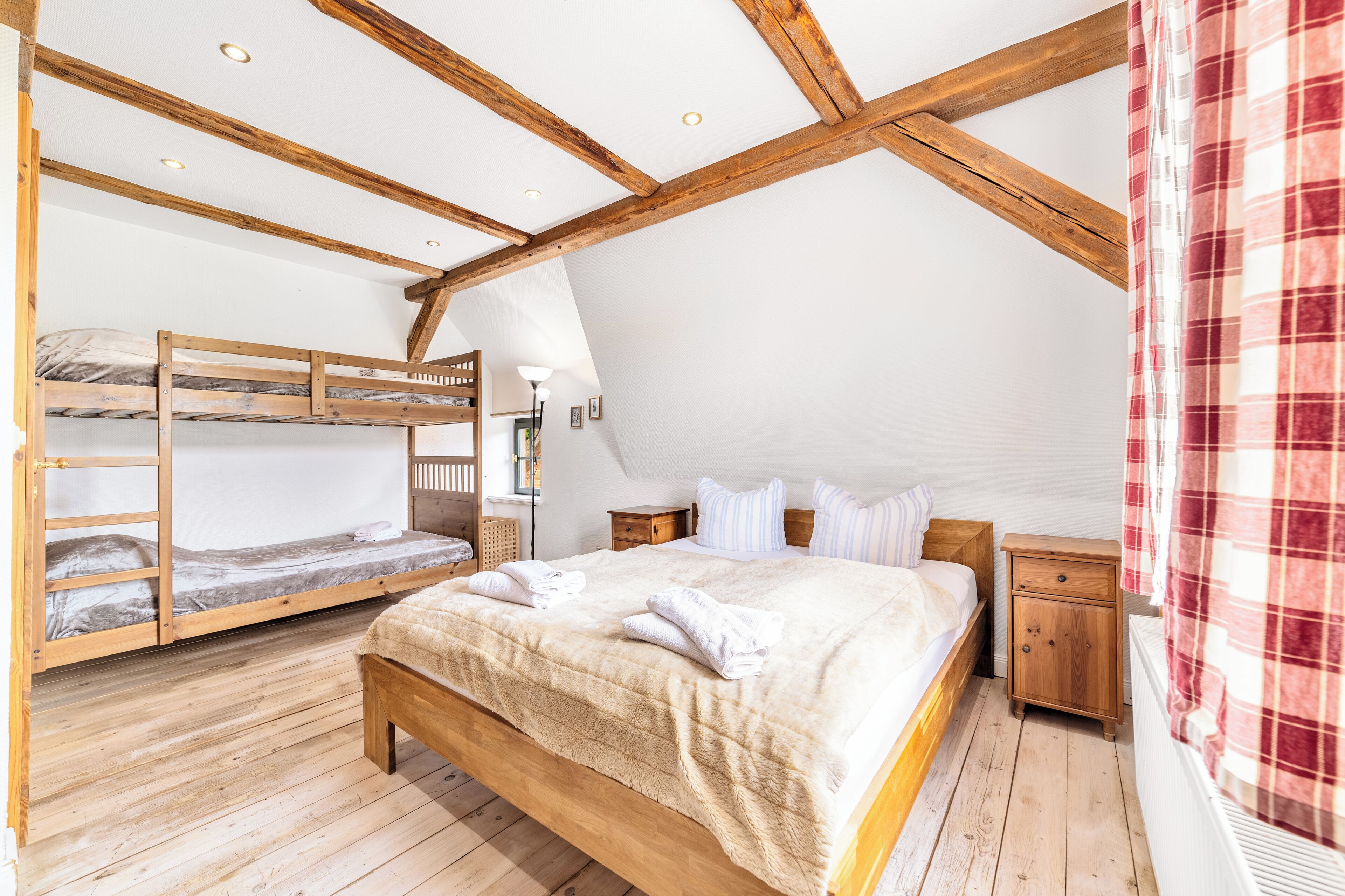 A bedroom with a bunk bed, a single bed, wooden flooring, and a sloped ceiling.