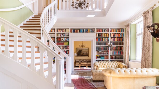 Amplia sala de estar con una escalera que conduce a un segundo piso, una gran estantería llena de libros, un sofá cómodo y una araña.