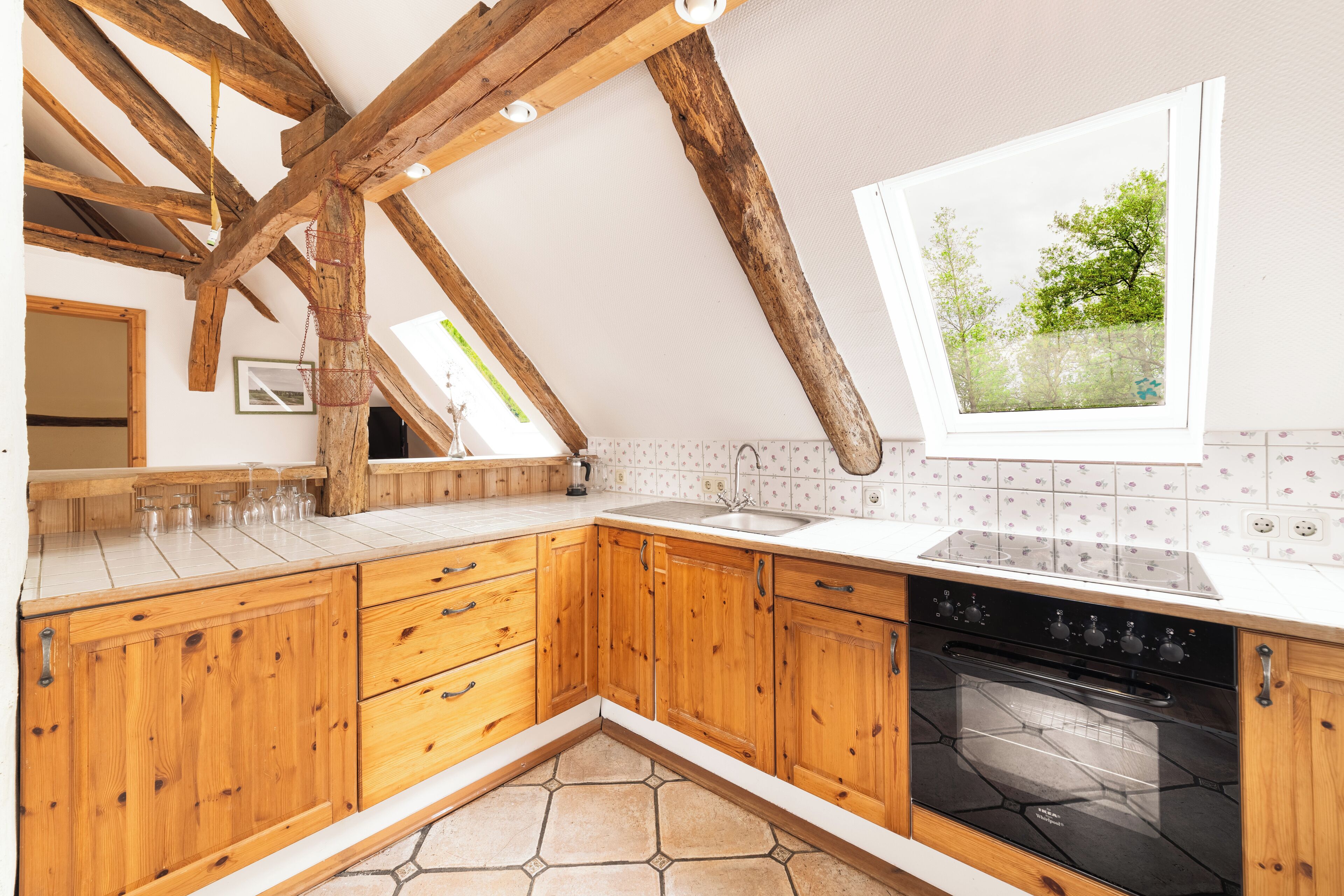 Une cuisine avec des meubles de rangement en bois, un four noir et une fenêtre donnant sur des arbres.