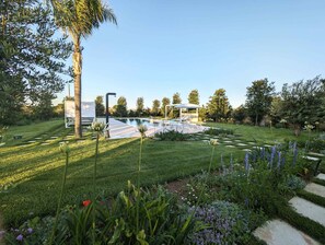 A modern outdoor pool area with a lounge chair and umbrella, surrounded by well-manicured lawns and flowering plants. - Alternative Relax Rooms by Oikia Vacanze (Scorrano)