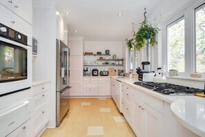 A modern kitchen with white cabinetry, a Bosch oven, a refrigerator, a stove, and a hanging plant.