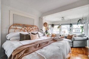 A bedroom with a large bed, a grey sofa, and a ceiling fan. - Century home by river, hot tub & parking (Ottawa)