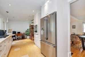 A modern kitchen with stainless steel appliances, a dining area with wooden chairs, and a workspace with a desk and computer. - Century home by river, hot tub & parking (Ottawa)