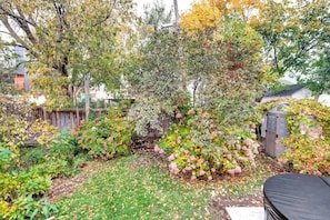 A backyard with a variety of plants and a wooden fence. - Century home by river, hot tub & parking (Ottawa)