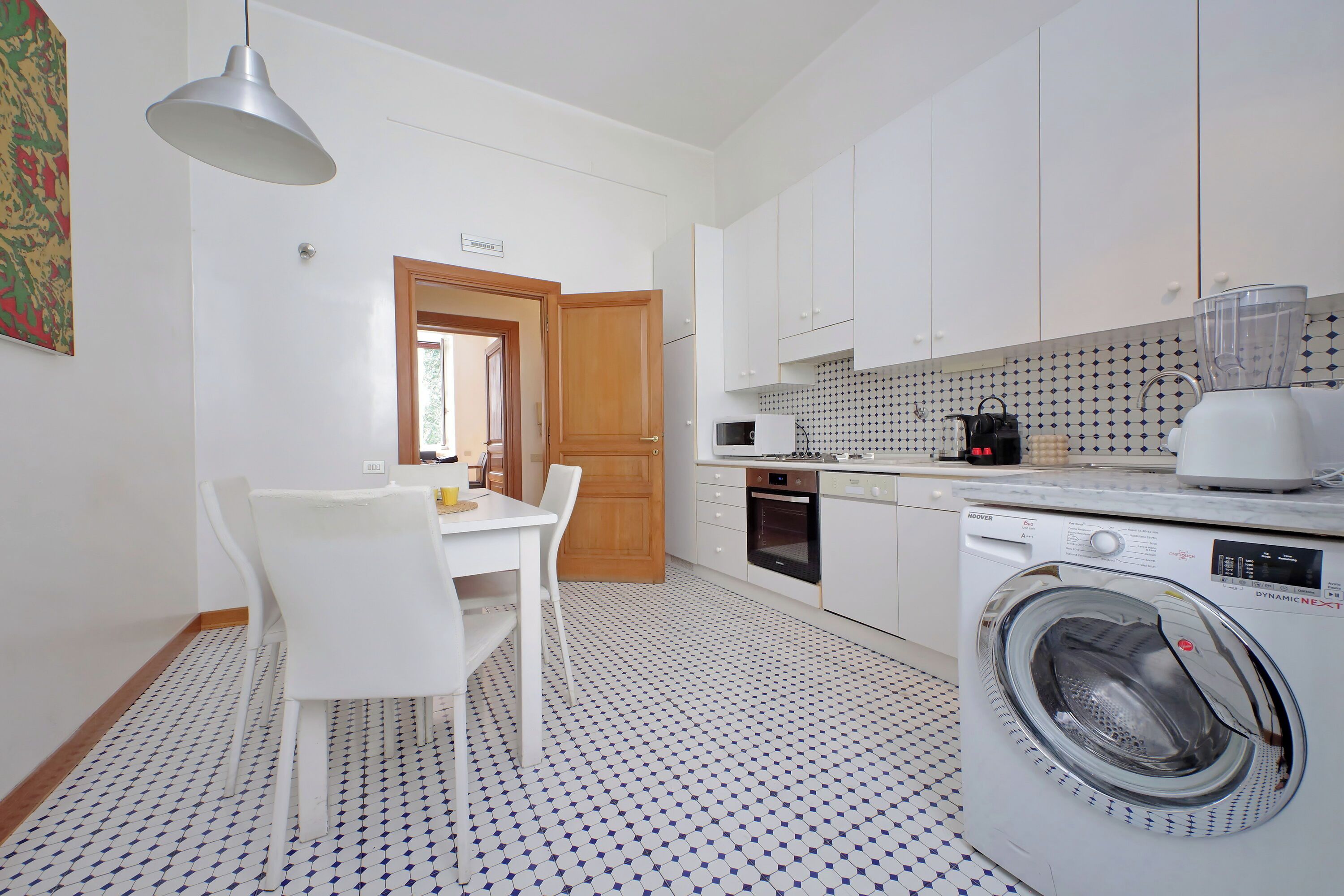 A compact kitchen with a washing machine, a dining table with chairs, and a pendant light.