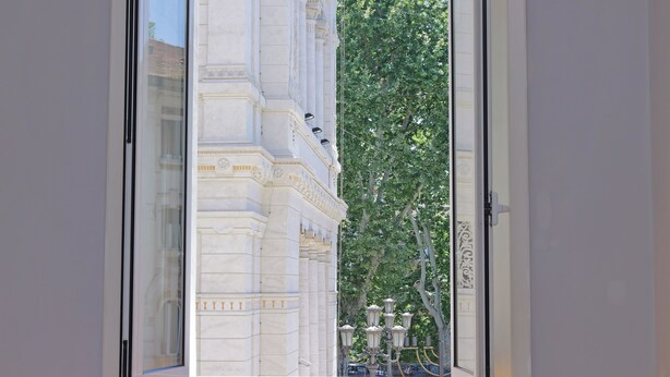 A view through a window of a building with classical architecture, including ornate columns and a balcony with a wrought iron railing. - Luxury home in the Ghetto's heart (Roma)