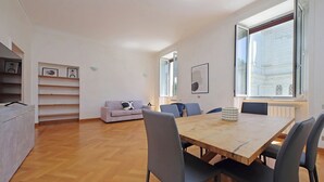 A modern living room with a wooden dining table, grey chairs, a sofa, and a TV on a stand. - Luxury home in the Ghetto's heart (Roma)