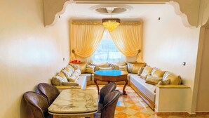 A dining area with a checkered floor, a round table, and a sofa set. - Appartement Meublé à Tanger, Parfait Pour les Familles (Tanger)