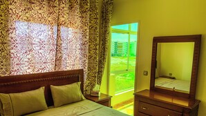 A bedroom with a bed, a dresser, a mirror, and a window with curtains. - Appartement Meublé à Tanger, Parfait Pour les Familles (Tanger)