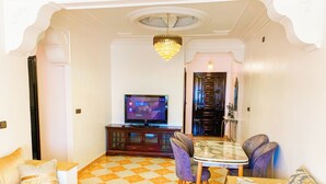 A living room with a checkered floor, a television, a dining table with chairs, and a sofa. - Appartement Meublé à Tanger, Parfait Pour les Familles (Tanger)