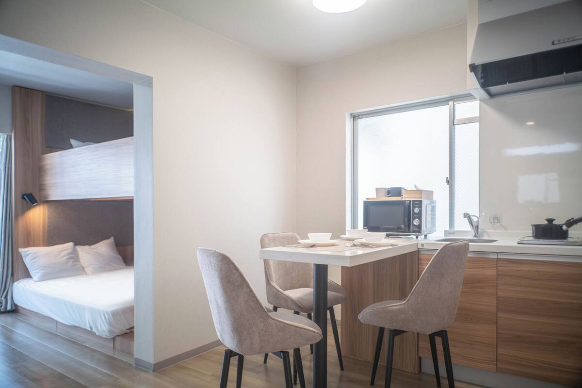A modern hotel room with a bunk bed, a dining area with a table and chairs, a microwave, and a sink.