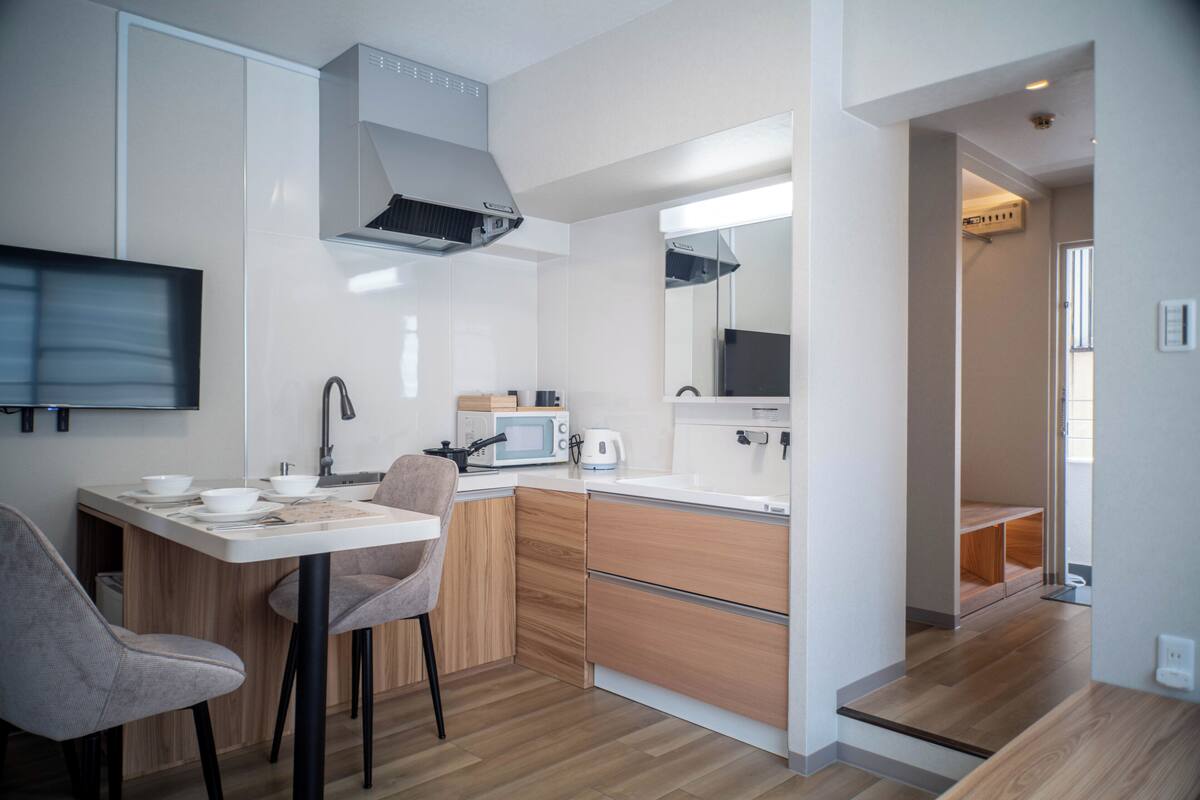 A modern kitchen with a dining area, wooden cabinets, a microwave, and a flat-screen TV.