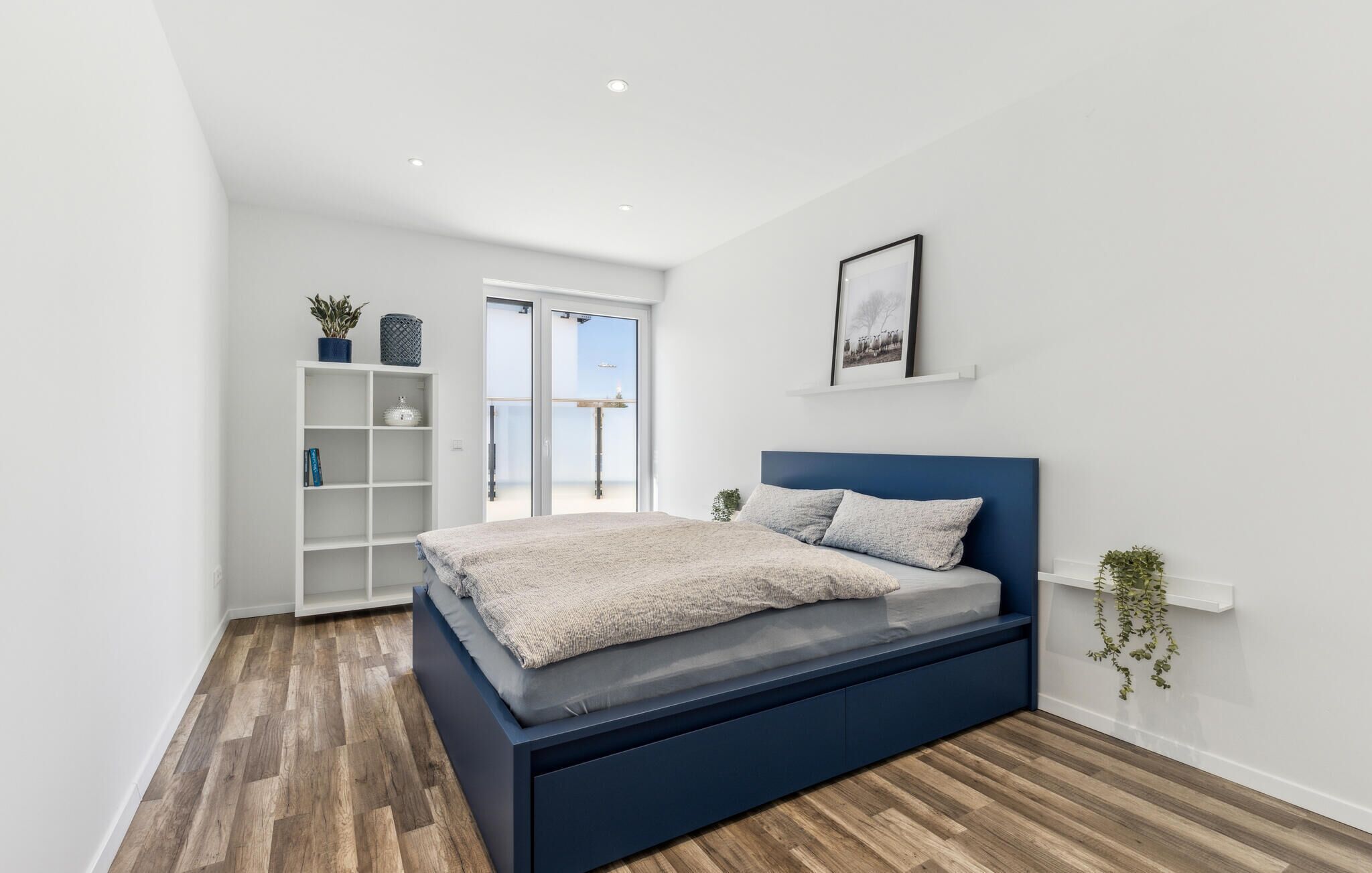 Une chambre moderne avec un lit, une étagère blanche et une vue à travers une porte vitrée.