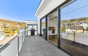Un balcon moderne offrant une vue sur un quartier résidentiel, avec un barbecue et une porte-fenêtre coulissante donnant sur la cuisine.