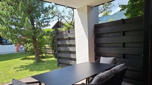 Un patio exterior con una mesa y sillas, una valla de madera y vistas a una casa y árboles.